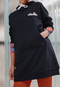 Sweatshirt à capuche noir avec une poche kangourou, arborant un logo blanc et des poignets à motifs colorés. Coupe décontractée, tissu au toucher doux.