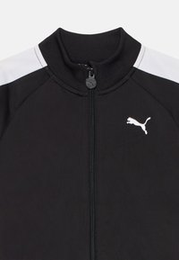 Svart Puma-jacka med dragkedja, hög krage och vita axelpartier. Har en liten vit Puma-logotyp på vänster bröstområde.