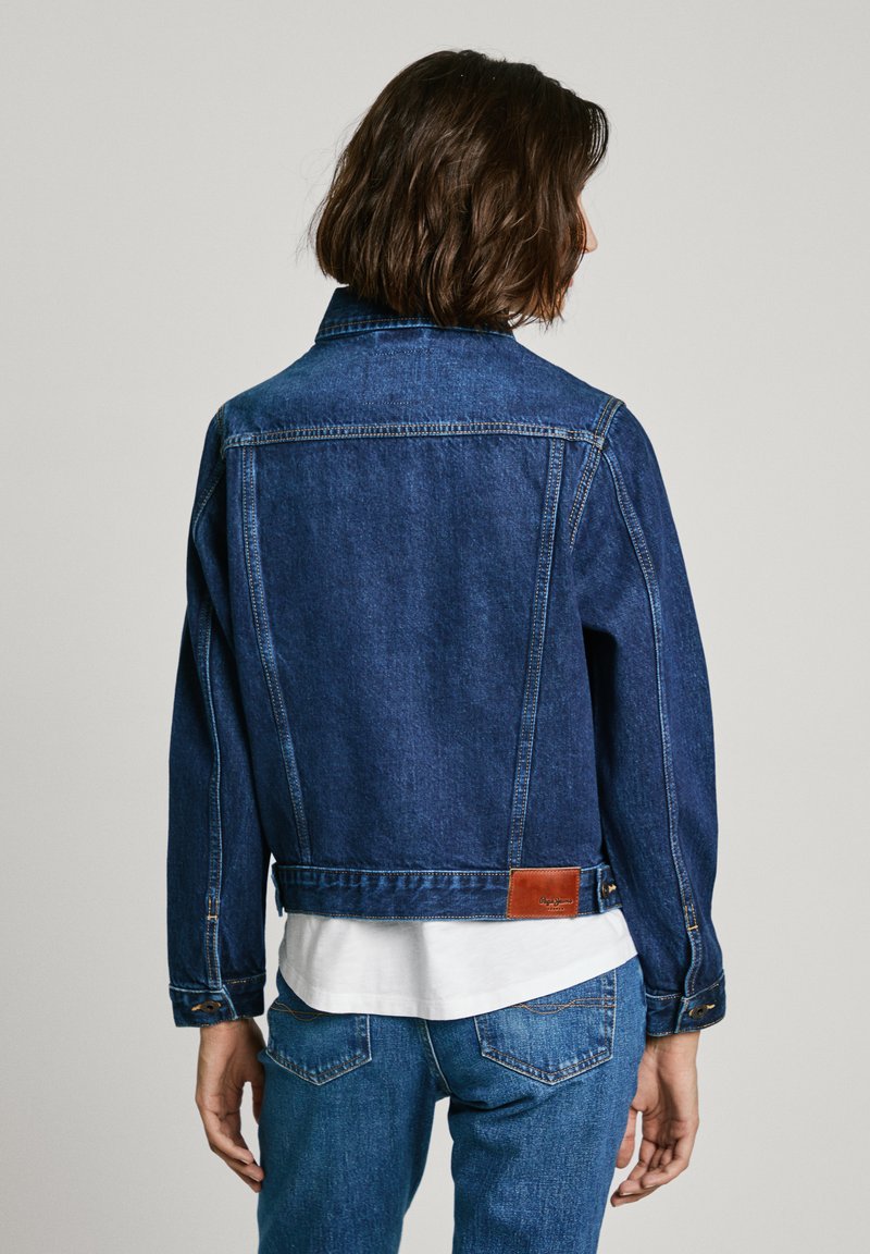 Chaqueta de mezclilla azul oscura con un diseño clásico, que presenta una parche de cuero en la parte posterior, puños abotonados y una longitud corta.
