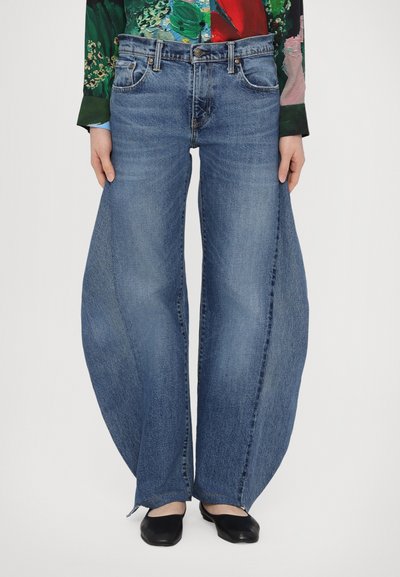 Jean en denim bleu clair avec un design large et évasé, comportant une braguette à boutons, cinq poches et une texture lisse.