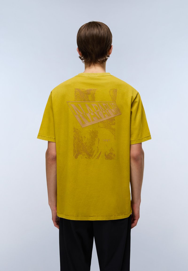 Gul bomulds T-shirt med en stor, tekstureret rød "NAPAPIJRI" grafik på ryggen, korte ærmer og rund hals.