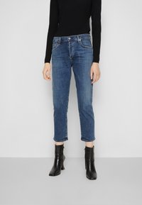 Blå denimjeans med rak ben, croppad längd och rå kant. Kombinerat med svarta högklackade ankelboots och en figurnära svart topp.