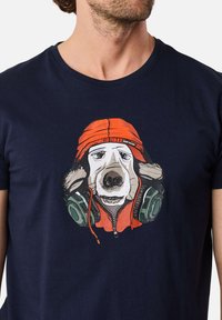Navyblaues T-Shirt mit einem Grafikdesign eines Hundes in einem orangefarbenen Hoodie mit Kopfhörern. Das Design ist auffällig mit detaillierten Gesichtszügen und Farben.