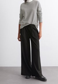 Maglione grigio in maglia waffle abbinato a pantaloni neri a gamba larga. Il maglione presenta maniche lunghe e un collo rotondo; i pantaloni hanno un elastico in vita.