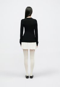 Bluză neagră cu mâneci lungi, cu textură rib, combinată cu o fustă crem. Dresuri albe și pantofi negri completează ținuta. Vedere din spate.
