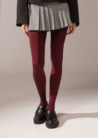 Bordeaux leggings parret med en sort jakke og en plisseret sort-hvid ternet nederdel, komplementeret af chunky sorte loafers.