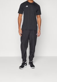 Svart träningsoutfit som består av en kortärmad topp med ränder och matchande avsmalnande byxor med sidodetaljer. Inkluderar svarta skor.