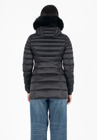 Giubbotto puffa nero con design a trapunte orizzontali, dotato di cappuccio in pelliccia sintetica e vita aderente. Abbinato a jeans blu a gamba larga.