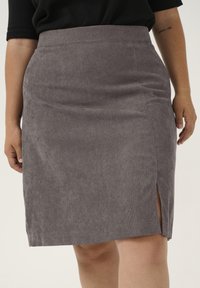 Jupe crayon en velours côtelé gris avec une fente latérale, présentant un léger effet de nervures verticales et une texture lisse. Design mi-long et ajusté.