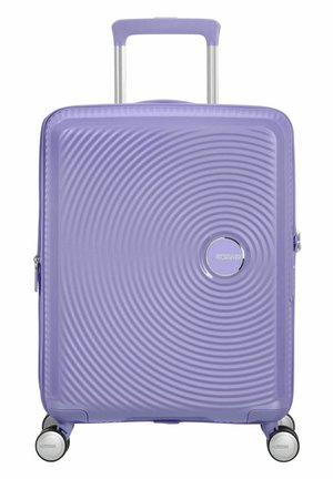 Hard-shell suitcase in lavender, featuring a textured wave pattern, silver logo, retractable handle, and four multicolor spinner wheels.