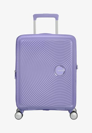 Valigia rigida di colore lavanda, con un motivo a onde testurizzate, logo argentato, manico telescopico e quattro ruote girevoli multicolori.
