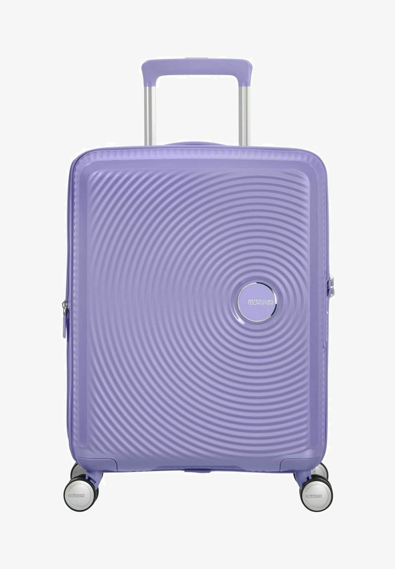 Valigia rigida di colore lavanda, con un motivo a onde testurizzate, logo argentato, manico telescopico e quattro ruote girevoli multicolori.