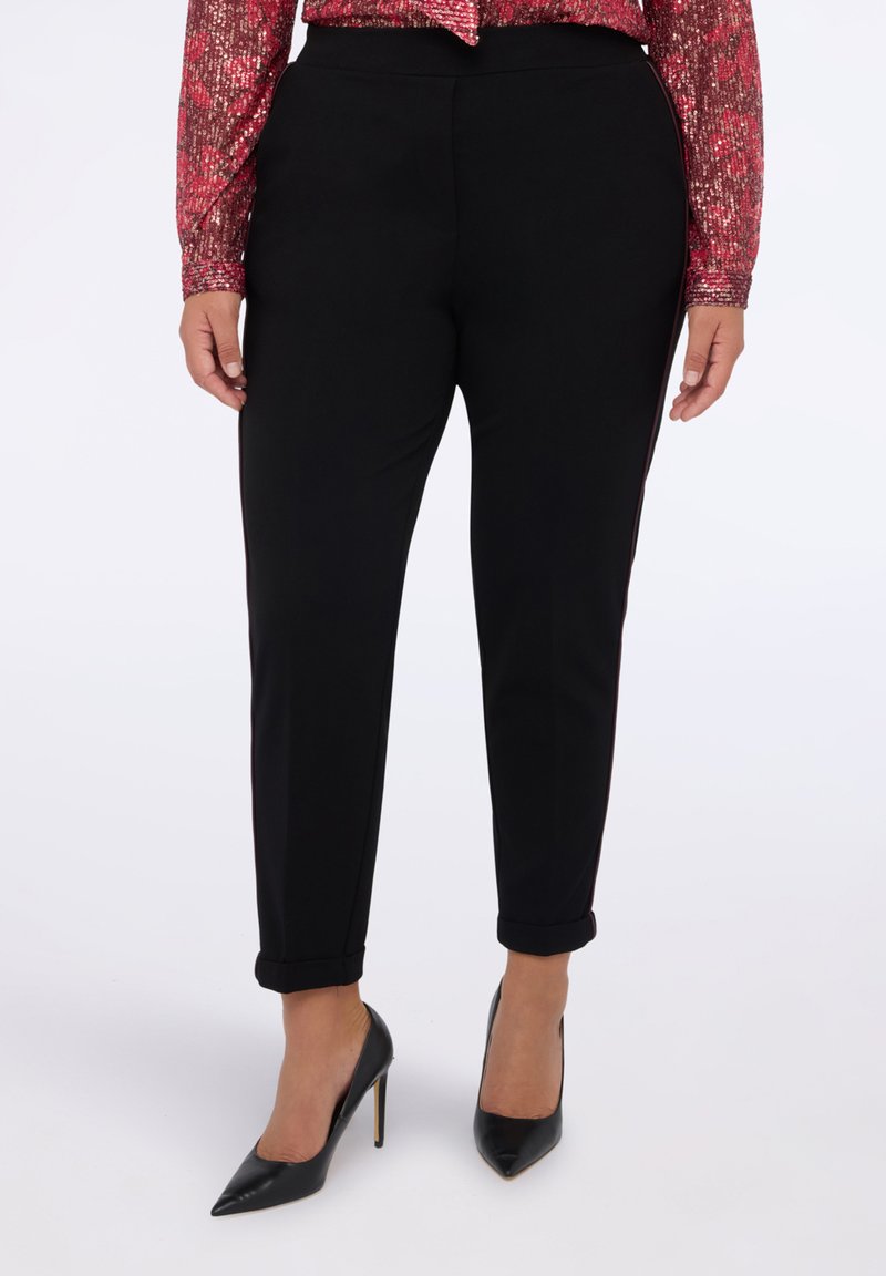 Pantalones tapered negros hechos de tela suave con cintura media, puños en los tobillos y una silueta elegante, combinados con tacones de aguja negros.