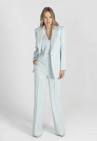 Jasnoniebieski garnitur trzyczęściowy wykonany z teksturowanej tkaniny. Posiada dopasowaną marynarkę, kamizelkę z guzikami oraz szerokie spodnie.