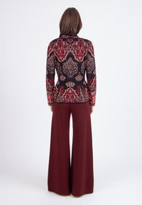 Blazer a fantasia nero e rosso con maniche lunghe, design peplum; abbinato a pantaloni larghi color bordeaux, texture liscia, vestibilità elegante.