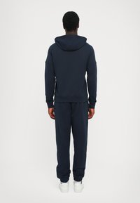 Felpa con cappuccio navy e pantaloni jogger abbinati, texture a maglia, polsini e orlo a coste, cappuccio arrotondato, sneakers bianche, design semplice senza motivi.