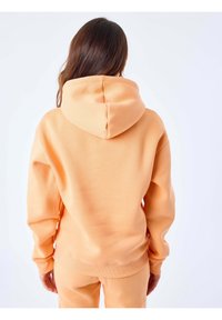 Perzikkleurige hoodie van zachte stof, met een trekkoordkap, ribgebreide manchetten en een relaxte pasvorm, gedragen met bijpassende broek.