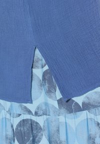 Tessuto blu texturizzato con uno spacco laterale, sovrapposto a un tessuto blu chiaro con motivi circolari scuri. Design sgualcito e fluido.