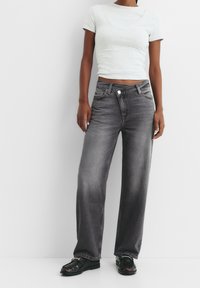 Sivé deninové nohavice širokého strihu s vyblednutým efektom, s gombíkovým zapínaním a klasickým dizajnom s piatimi vreckami, v kombinácii s priliehavou svetlosivou košeľou.