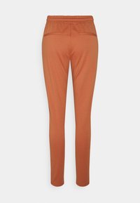 Joggers de color óxido con cinturilla elástica, piernas ajustadas y dos bolsillos traseros. La tela parece suave con un ligero brillo.