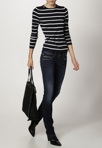 Marinblå och vit randig långärmad topp med axel detaljer, ihopparad med mörkblå jeans och en svart tote-väska, kompletterad med svarta klackar.