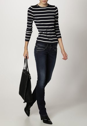 Top de rayas azul marino y blanco de manga larga con acentos en los hombros, combinado con jeans azul oscuro y un bolso tote negro, complementado con tacones negros.