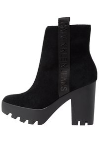 Svarta mocka anklar stövlar med en kraftig klack, utrustade med ett strukturerat svart logoband på sidan och en robust, mönstrad plattformssula.