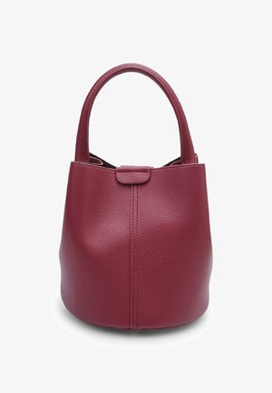 Round, burgundy leather bag with textured surface, short handles, and a minimalistic design. Closure tab at the front.
