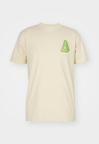 Camiseta de algodón beige con un gráfico de triángulo verde en el lado izquierdo del pecho. Mangas cortas y cuello redondo. Textura suave.