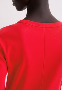 Czerwona bluzka z długim rękawem, okrągłym dekoltem i gładką teksturą, z centralnym szwem z tyłu i dopasowanymi rękawami.