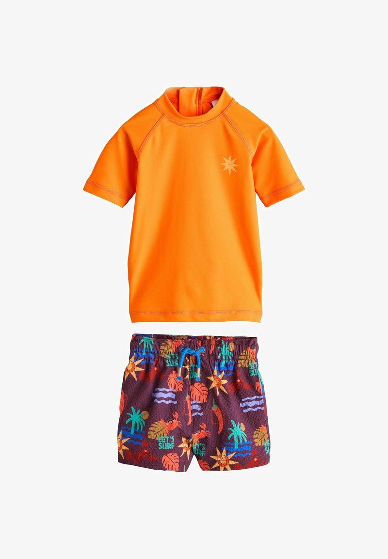 Maglietta da surf arancione brillante a maniche corte con logo del sole abbinata a pantaloncini da nuoto scuri con stampe colorate a tema tropicale e surf.