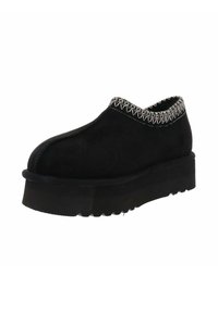 Zapato negro de ante tipo slip-on con punta redonda, costura plateada texturizada a lo largo del collar y suela gruesa y estriada.