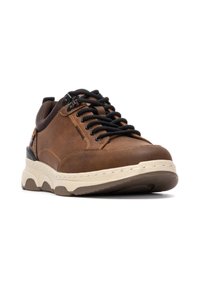 Zapatilla de cuero marrón con cordones negros, detalles texturizados y una media suela blanca. Presenta una puntera redondeada y una suela robusta para mejor agarre.