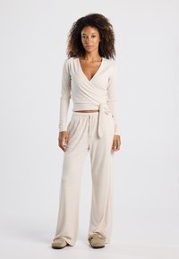 Beige wrap top with long sleeves and deep V-neck paired with loose-fitting pants. Soft fabric with a smooth texture. Tie at the waist.
