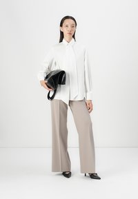 White long-sleeve button-up shirt, beige wide-leg pants, holding a black textured handbag, with black pointed-toe heels, minimalistic design.