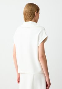 Witte, korte mouw top met een opgerolde kraag, gemaakt van gladde stof. Beschikt over een minimalistisch ontwerp en een relaxte pasvorm, bekeken vanuit de achterkant.