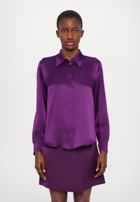 Lilla satin skjorte med knapper, krave, lange ærmer og en let buet kant, parret med en matchende lilla nederdel.