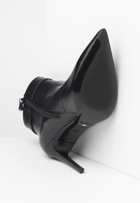 Black leather ankle boot with a pointed toe, high stiletto heel, side zipper, and textured sole. Label indicates size 37, made in Italy.