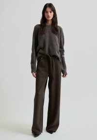 Maglione grigio a maglia con una vestibilità rilassata, abbinato a pantaloni larghi a vita alta di un marrone scuro e calzature nere a punta.