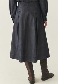 Spódnica dżinsowa w ciemnoniebieskim kolorze, z przodu z zakładkami i rozkloszowanym fasonem. Połączona z brązowymi, wysokimi kozakami do kolan, podkreślającymi fakturę i sylwetkę.