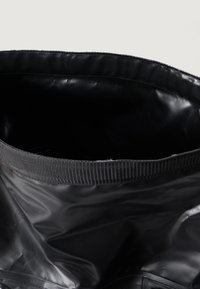 Saco preto com uma superfície lisa e brilhante e uma borda superior texturizada e elástica. O interior parece espaçoso e totalmente forrado.