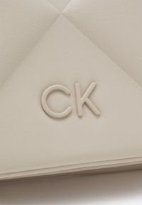 Clutch in finta pelle bianca con finitura testurizzata. Presenta un logo "CK" in rilievo e un design a pannello triangolare. Aspetto minimalista ed elegante.