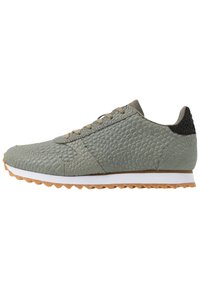 Harmaa rakenne kengät kumipohjalla, varustettuna pyöreällä varpaalla, nauhakiinnityksellä ja mustalla korostuksella kantapäässä. Valkoinen välikerros.