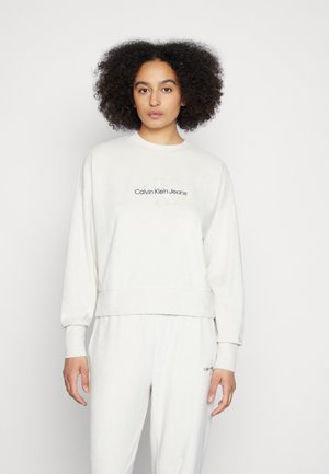 Kerge beež dressipluus pikkade varrukatega, ribatud soonikutega ja lühendatud hemiga. Rinnal on tumehall "Calvin Klein Jeans" logo.