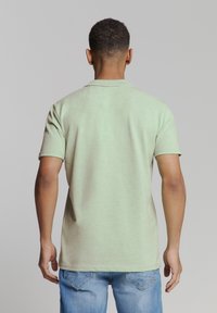 Lichtgroen polo-shirt met korte mouwen en een kraag, met een ontspannen pasvorm, gecombineerd met lichtblauwe denim jeans. Gladde textuur, geen zichtbare patronen.