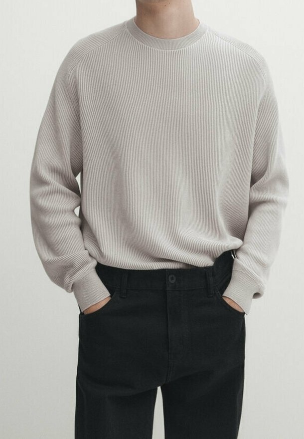 Pull en maille côtelée beige clair avec un col rond, associé à un pantalon noir. Le pull a des manches longues et une coupe décontractée.