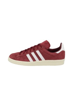 Røde ruskindsneakers med hvide striber, der har et low-top design, rund tå og tekstureret materiale. Tykk gummisål. Snørelukning.