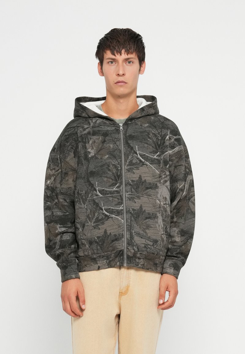 Mikina s kapucňou na zips v tmavo sivej farbe, s dizajnom v tvare listov. Vyrobená z mäkkej tkaniny s textúrovaným povrchom.