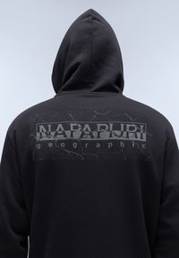 Mustapaitahuppari, jossa on halkeillut graafinen printti, jossa takana on tekstit "Napapijri" ja "geographic". Sujuva kangaslaatu.