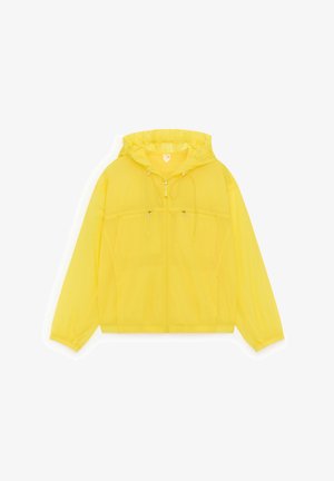 Žuta lagana jakna s kapuljačom, prednjim patentnim zatvaračem, vrpcama za podešavanje i džepovima na prsima s patentnim zatvaračima, prikazana ravno na bijeloj pozadini.
